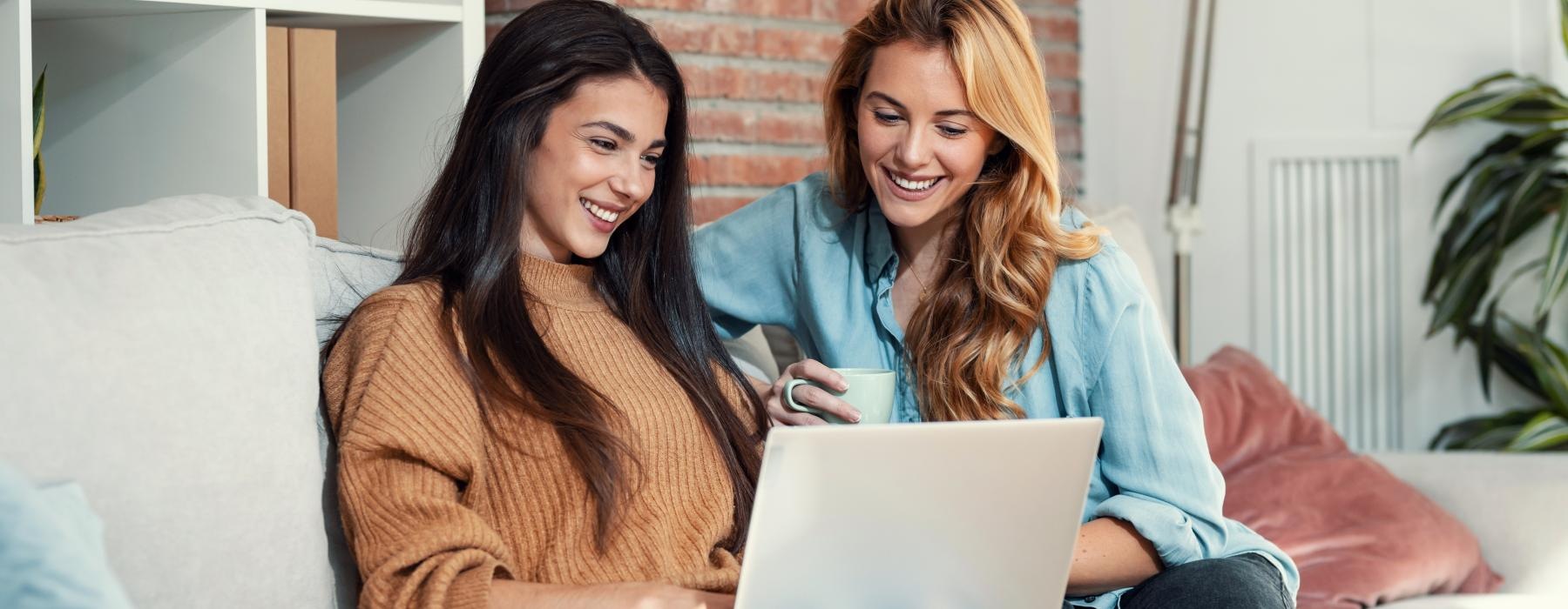 a couple of women sitting on a couch looking at a laptop