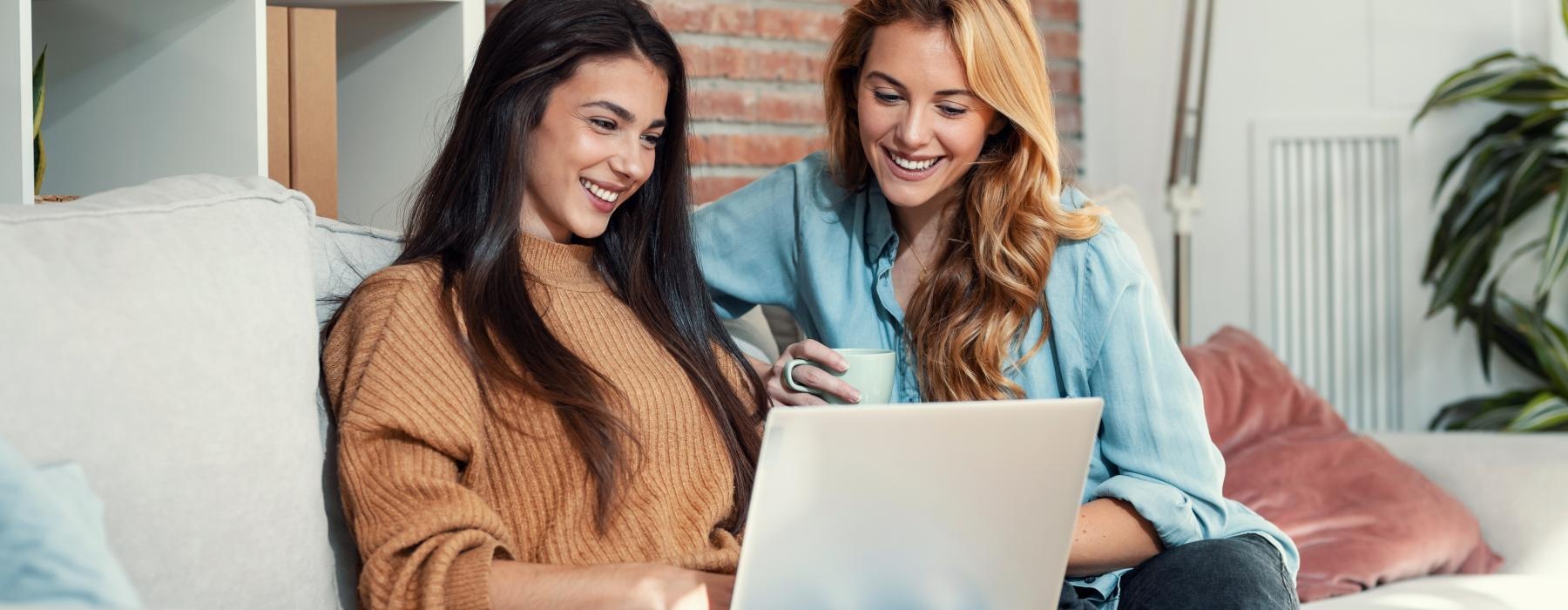 a couple of women sitting on a couch looking at a laptop